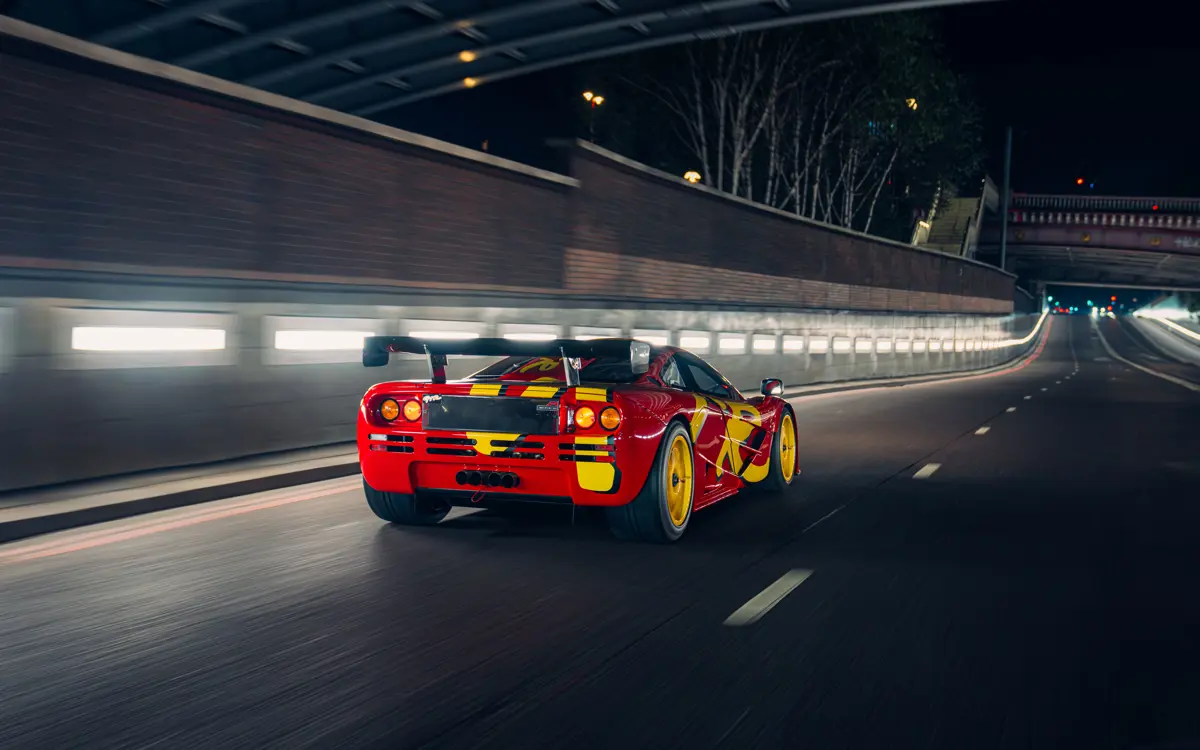 Rear view of the 1996 McLaren F1 GTR driving through a city illuminated by streetlights.