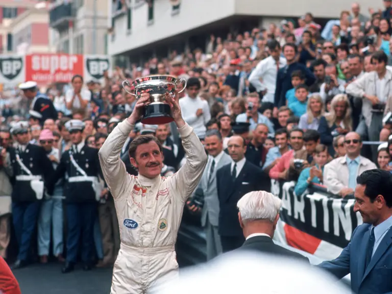 Graham Hill triumphantly raises his 1st-place trophy after having secured victory at the 1969 Monaco Grand Prix.