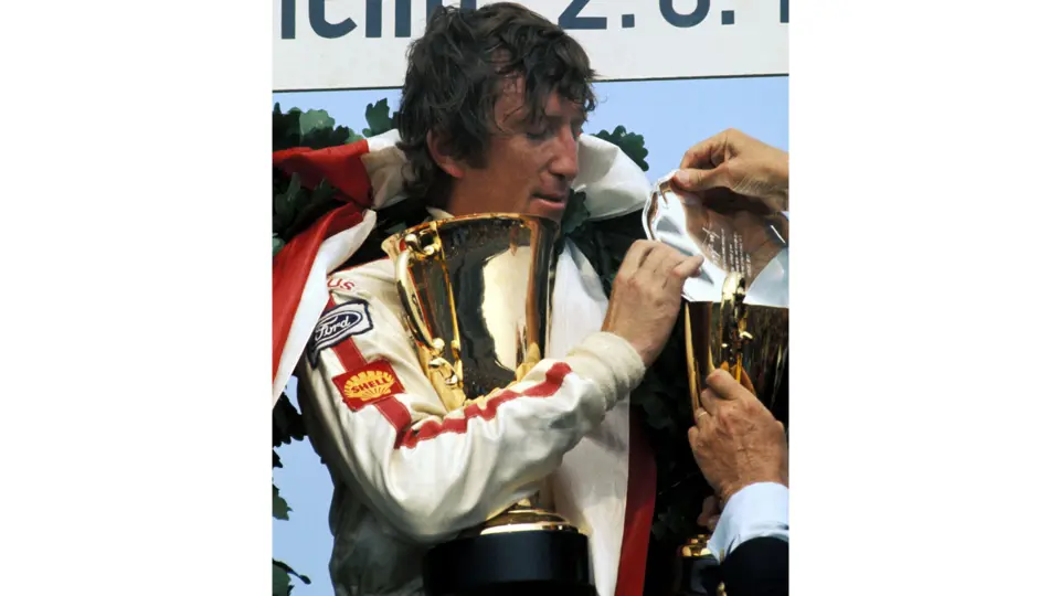 Jochen Rindt stands on the podium holding his final 1st-place trophy at the 1970 German Grand Prix. This victory would secure his World Championship later that year.