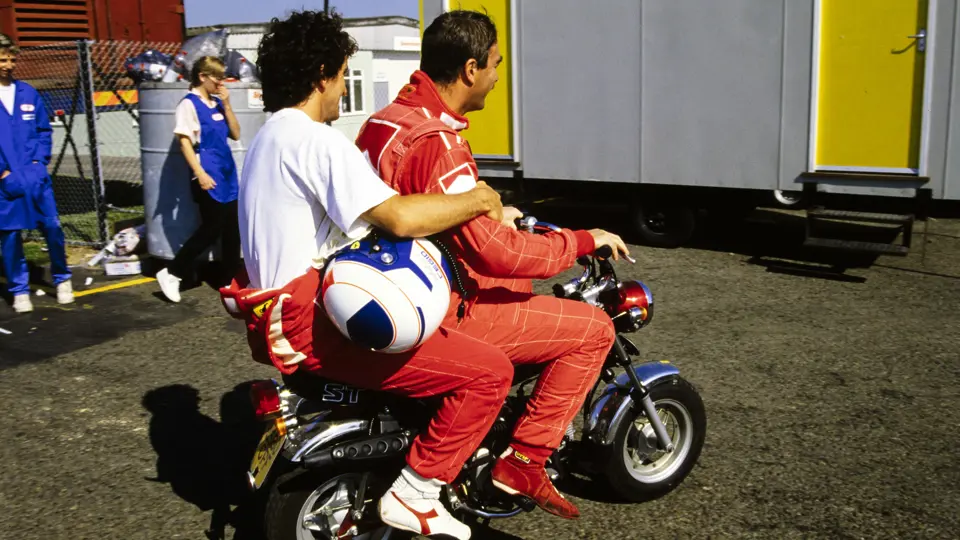 Nigel Mansell gives his Scuderia Ferrari co-driver Alain Prost a ride on his Honda ST-70 motorbike at the 1990 British Grand Prix, which Prost won.