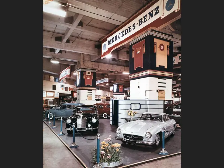 A colour photo shows chassis 4500012 on the 1954 Earls Court Motor Show stand alongside a Mercedes-Benz 220.