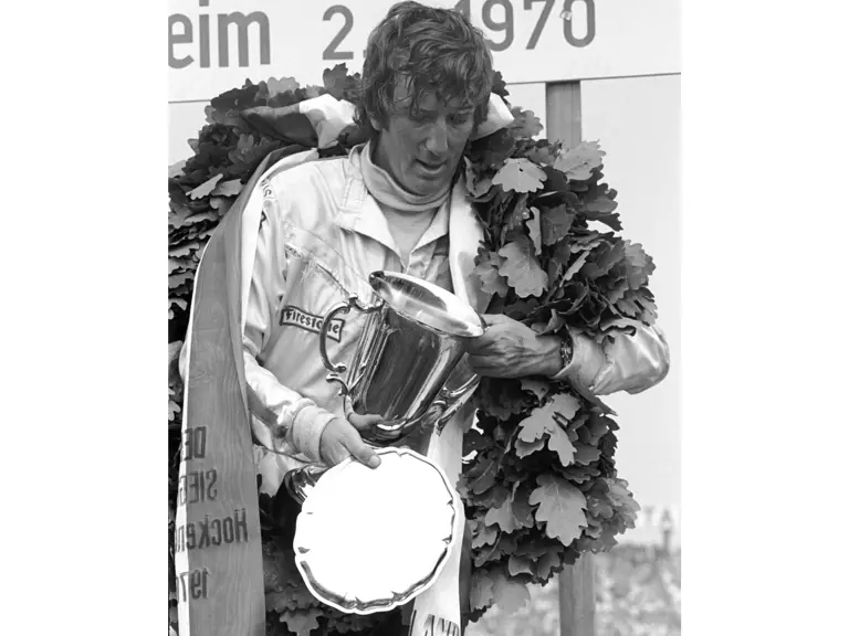 Jochen Rindt stands on the podium holding his final 1st-place trophy at the 1970 German Grand Prix. This victory would secure his World Championship later that year.