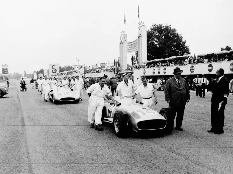 Mechanics push the four Mercedes-Benz W 196 R racing cars at the start of training laps before the 1955 Formula One Grand Prix at Monza. Two streamlined cars and two open-wheel cars were used for the race. Race director Albert Neubauer stands at the front of the first car. Chassis number 00009/54, in Streamliner configuration, is the second car, #16. 