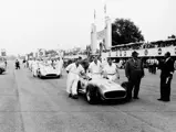 Mechanics push the four Mercedes-Benz W 196 R racing cars at the start of training laps before the 1955 Formula One Grand Prix at Monza. Two streamlined cars and two open-wheel cars were used for the race. Race director Albert Neubauer stands at the front of the first car. Chassis number 00009/54, in Streamliner configuration, is the second car, #16. 