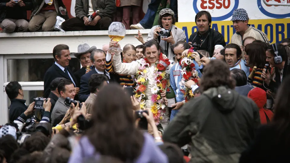 Winner of the 1972 24 Hours of Le Mans, Graham Hill, triumphantly raises his glass trophy filled with champagne to celebrate his victory. Winner of the 1972 24 Hours of Le Mans, Graham Hill, triumphantly raises his glass trophy filled with champagne to celebrate his victory.