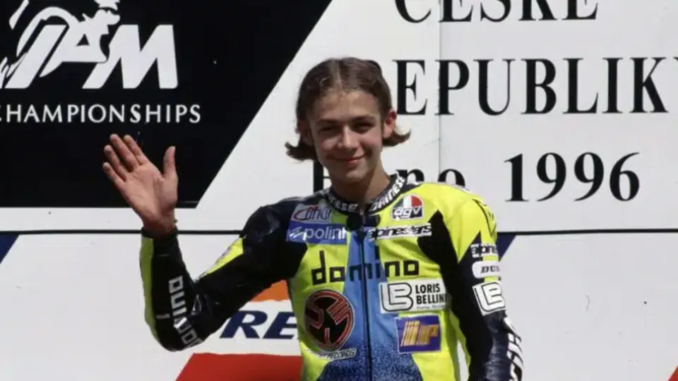 A 17-year-old Valentino Rossi waves on the podium as he awaits his first-place trophy at the 1996 Czech Grand Prix.
