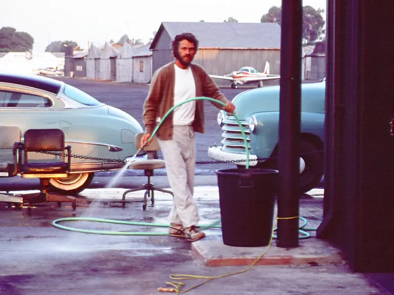 Steve McQueen with his 1952 Hudson Wasp proudly parked outside his hanger at the Santa Paula airport.