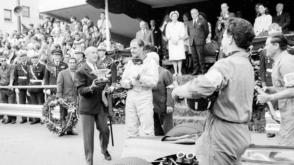 Graham Hill clasping his glass trophy for setting the fastest lap at the 1965 Monaco Grand Prix.