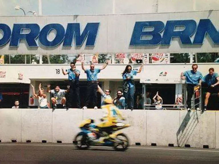 Having just crossed the finish line, Rossi’s teammates cheer from the paddock to celebrate the rookie’s first victory at the 1996 Czech Grand Prix.