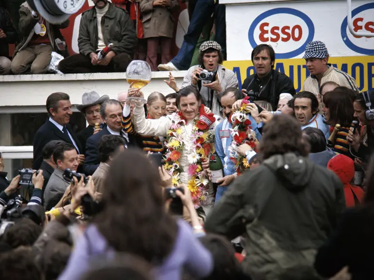 Winner of the 1972 24 Hours of Le Mans, Graham Hill, triumphantly raises his glass trophy filled with champagne to celebrate his victory.