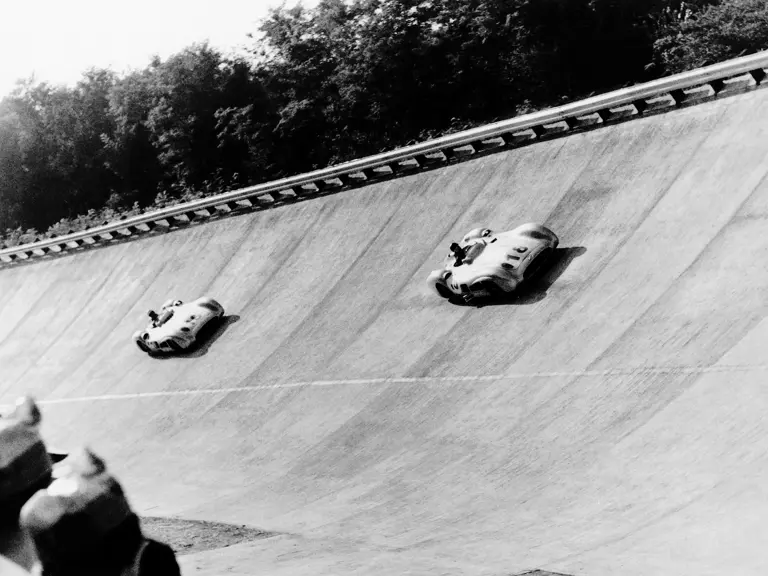 Italian Grand Prix at Monza, 11 September 1955. Eventual winner Juan Manuel Fangio (#18) is followed by Stirling Moss (#16, chassis number 00009/54); in the famous banked turn. Both are in Mercedes-Benz Formula One W 196 R racing cars with streamlined bodywork.