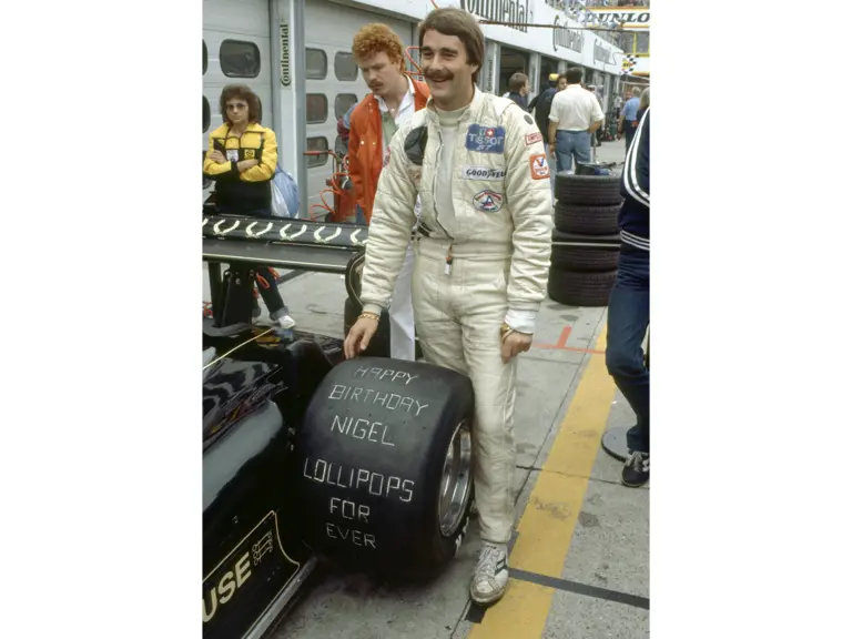 Nigel Mansell poses next to his Lotus 91 on his 29th birthday at the 1982 German Grand Prix. The engraved wheel seen in the image is available in this lot.