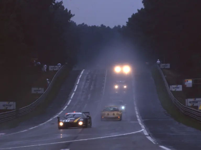 The Jaguar XJ220 C LM driven by Richard Piper, Tiff Needell, and James Weaver leads down the hill as night falls on the 1995 24 Hours of Le Mans.
