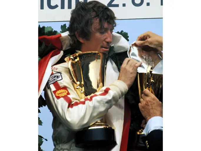 Jochen Rindt stands on the podium holding his final 1st-place trophy at the 1970 German Grand Prix. This victory would secure his World Championship later that year.
