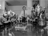 Graham Hill poses for a press photo with a selection of his trophies, on the far right at the front is his trophy for finishing 1st at the 1968 Mexican Grand Prix.