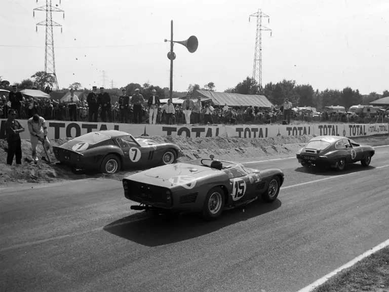 CIRCUIT DE LA SARTHE, FRANCE - JUNE 24: Maurice Charles / John Coundley, Jaguar E-type, leads Joakim Bonnier / Dan Gurney, Scuderia SSS Republica di Venezia, Ferrari 250 TRI/61, past Mike Parkes / Lorenzo Bandini, SpA Ferrari SEFAC, Ferrari 330 LM/GTO, beached by the side of the track during the 24 Hours of Le Mans at Circuit de la Sarthe on June 24, 1962 in Circuit de la Sarthe, France. (Photo by LAT Images)